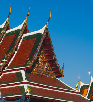 Ornate Multi-Tiered Temple Roof and Gilded Gable of Wat Arun Against Clear Blue Sky in Bangkok Thailand