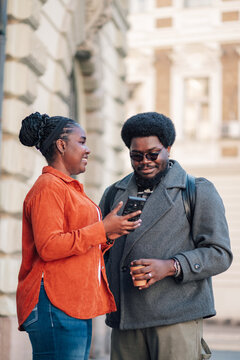 Young diverse couple looking at a mobile phone screen on a city street, sharing content, and communicating