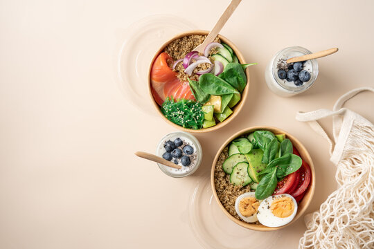 Healthy protein bowls with smoked salmon, egg, quinoa, avocado, spinach, cucumber and chuka seaweed salad in cardboard containers, served with chia seed yogurt and blueberries in glass jars 