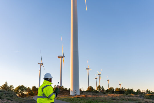 Engineer working at wind farm overseeing renewable energy production, using walkie-talkie for communication