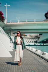 Fototapeta premium Woman walking, talking on smartphone, holding coffee cup in sunny valencia, spain, modern city street background