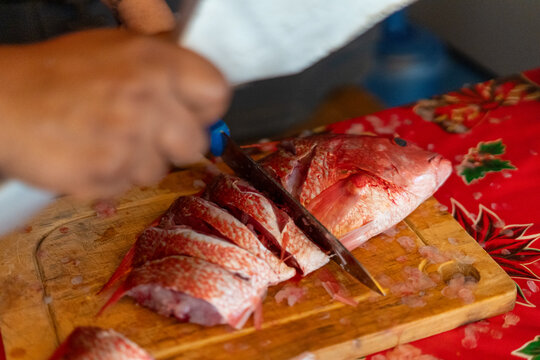 Hands slicing fresh red snapper on a wooden board, preparing seafood for a meal