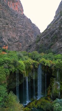 Slow upward camera movement reveals the mountain landscape and sky above Yerkopru Waterfall in Mersin, Turkiye, gradually widening the view from the cascading water to the surrounding green canyon and