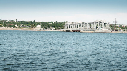 Fototapeta premium Hydroelectric power station viewed from the reservoir side with dam water and industrial infrastructure. Renewable energy and electricity generation concept