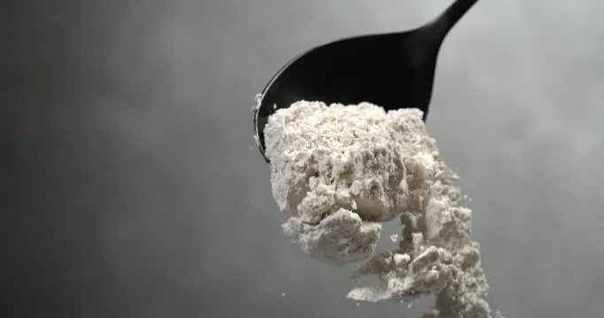 Dry milk powder falling from black spoon in super slow motion