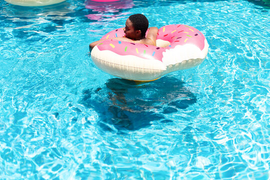Young Black man relaxing in a pink donut float in a clear blue pool