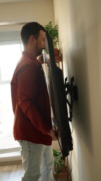 Concentrated homeowner carefully installing a new flatscreen television, precisely mounting the large smart tv onto an articulated bracket on the living room wall for home improvement
