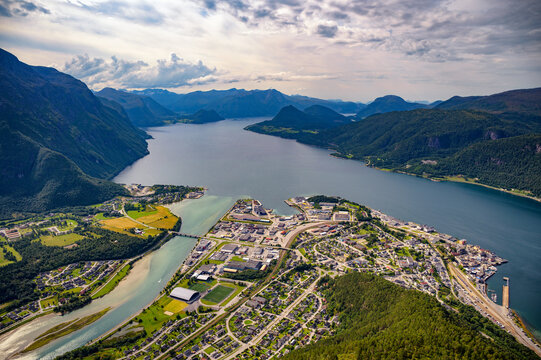 Scenic aerial view of Andalsnes with the Rauma River meeting Romsdalsfjord, framed by steep Romsdal mountains and dramatic clouds, seen from Nesaksla mountain in Norway.