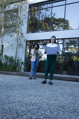 Two female colleagues in business attire holding plans, walking, talking on phone at glass facade © WavebreakMediaMicro