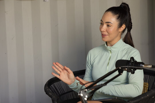 Adult woman sitting in chair in studio, wearing mint zip-up, speaking into boom-mic, copy space