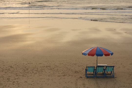 Minimalist high angle view of a red and blue umbrella with deck chairs on a sandy beach at sunset.
