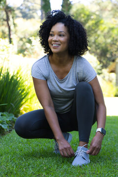 African adult woman crouching tying grey shoe laces in park wearing black leggings and smartwatch