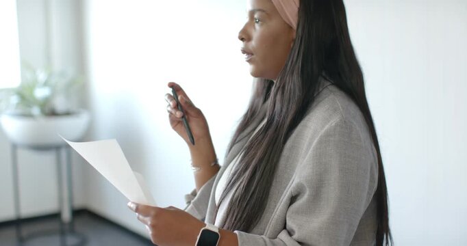 African American woman holding sheet and pen, starting practicing talk by scanning page near window
