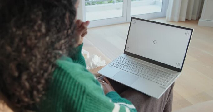 Woman is reacting on couch to laptop, gesturing, wiping nose with tissue while staying engaged