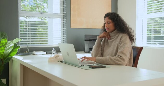 African American woman typing on laptop at desk, pausing, reading message on phone, copy space