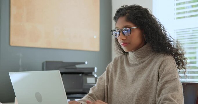 African American woman in tan top viewing laptop, adjusting specs, typing, taking notes in notebook
