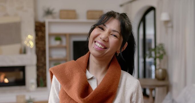 Facing camera, African American woman laughing and tilting head in living room with lit fireplace