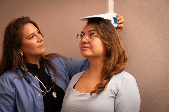 A female doctor measures a standing patient's height with a stadiometer during a routine medical checkup in a clinic.
