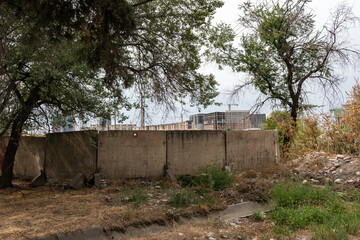 Urban development and construction boom in Bishkek, Kyrgyzstan, with new high-rise buildings rising behind an old concrete fence in a green area. © Dina Luk