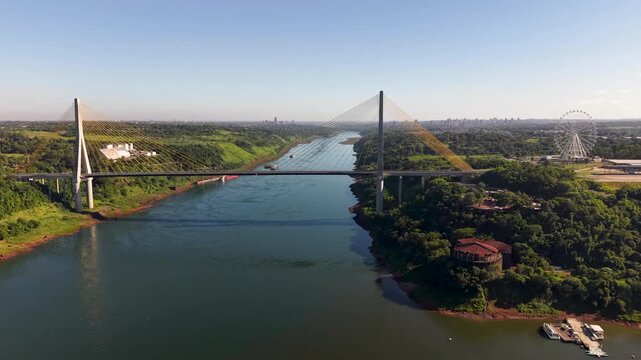 Aerial view of the International Friendship Bridge connecting Foz do Igua&ccedil;u, Brazil, and Ciudad del Este, Paraguay. Spans the Paran&aacute; River, with lush green banks and a ferris wheel