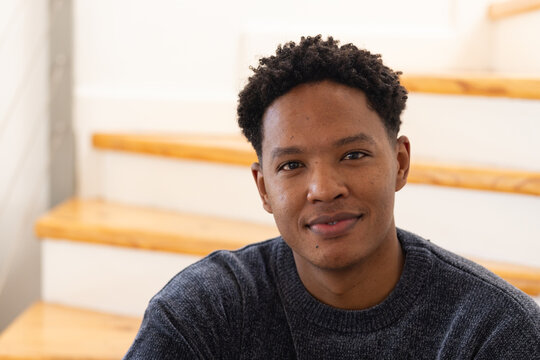 African American man sitting on wooden stairs in home stairwell, wearing dark gray knit sweater