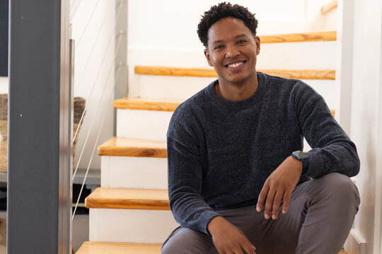 African American man sitting on wooden stairs with white risers, cable railing, wearing smartwatch