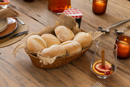 Woven oval basket is sitting on wooden table and is holding six floured crusty rolls