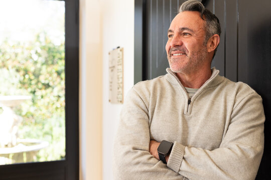 Middle-aged man standing with arms crossed in entryway, wearing quarter-zip sweater and smartwatch