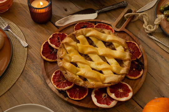 Lattice-top fruit pie is sitting on wooden board on dining table with candlelight and star anise