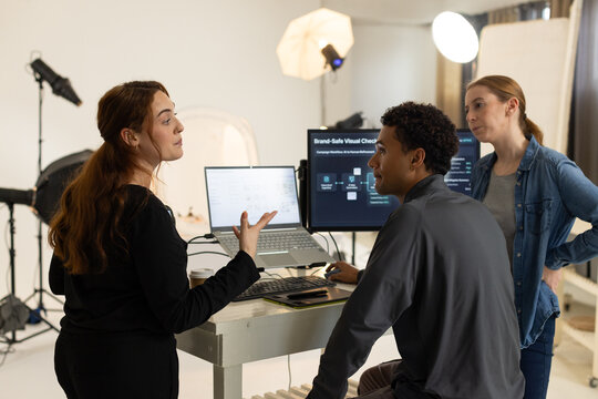 Diverse coworkers debating and editing visuals in studio with laptop, monitor and softbox