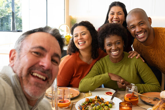 Five friends gathering around wooden dining table at home, holding smartphone and citrus drinks