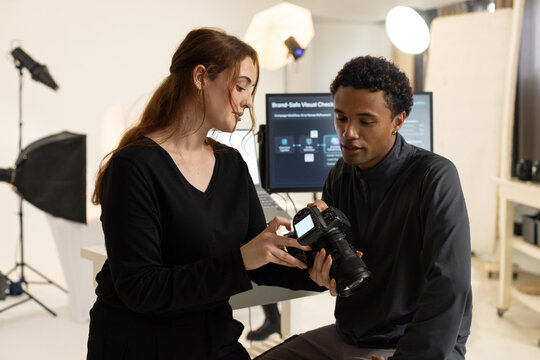 Diverse coworkers examining DSLR camera at photography studio, woman wearing black top checking LCD