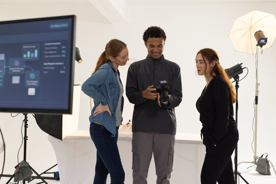 Diverse coworkers reviewing shots on DSLR camera in studio with umbrella light and monitor