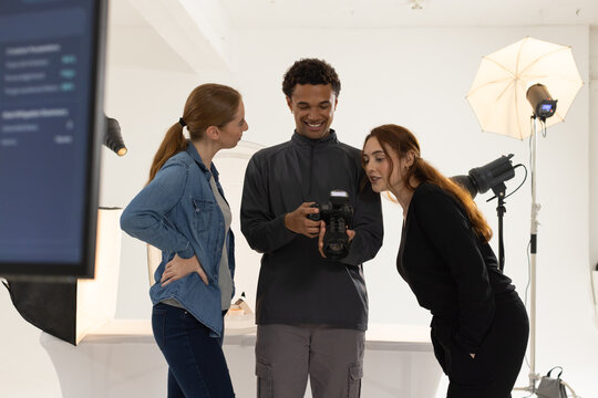 Diverse creative team reviewing DSLR camera with external flash on monitor in white studio