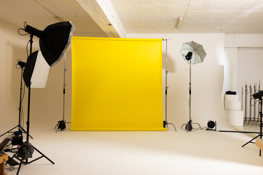 Yellow seamless backdrop is sweeping onto white cyclorama floor in studio with softbox, umbrella