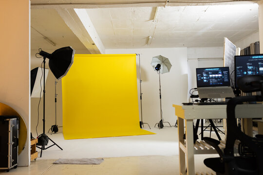 Yellow seamless backdrop rolling on stand in studio, softbox, umbrella lights, monitor showing UI