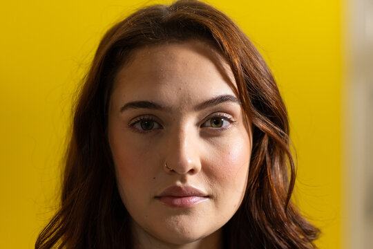 Adult female posing in studio against yellow backdrop, showing small hoop nose ring and wavy hair