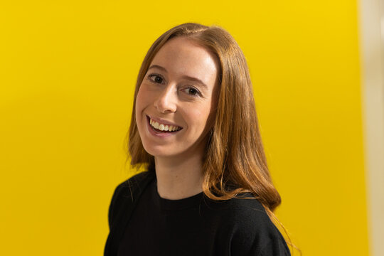 Adult woman smiling and posing against bright yellow backdrop while wearing plain black top