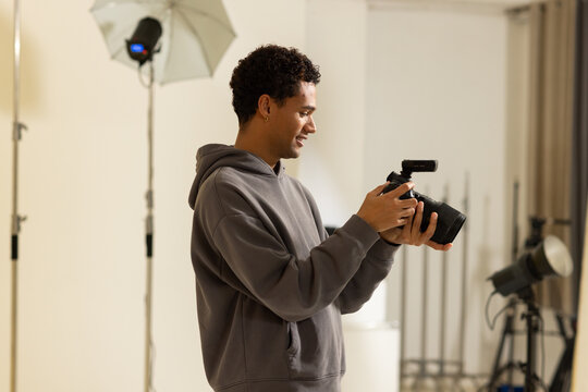 African American man wearing gray hoodie holding DSLR with flash while reviewing shots near softbox