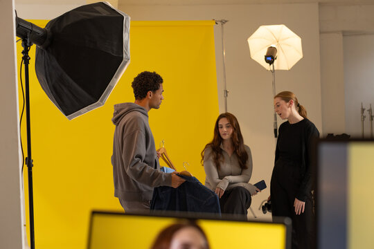 Diverse team evaluating garment hangers and smartphone on yellow backdrop in studio with softbox