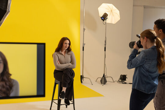 Female model with photographer and assistant posing on tall stool in studio with yellow paper DSLR
