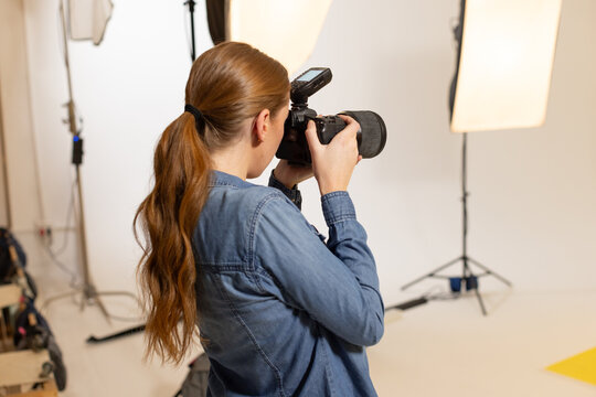 Female camera operator standing in studio holding DSLR with telephoto lens and external flash