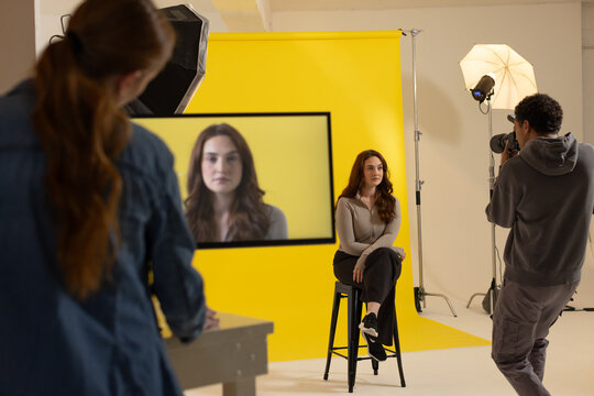 Team in studio shooting portrait, African American photog holding DSLR, monitor and yellow backdrop