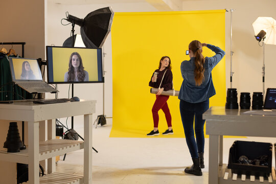 Female collaborators posing near yellow backdrop in studio, shooting with smartphone and prop tube