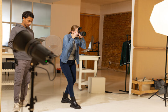 Diverse coworkers composing shot in loft studio, photographer wearing denim jacket holding DSLR