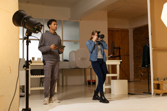 Diverse coworkers holding DSLR and tablet, adjusting strobe and softbox in photography studio