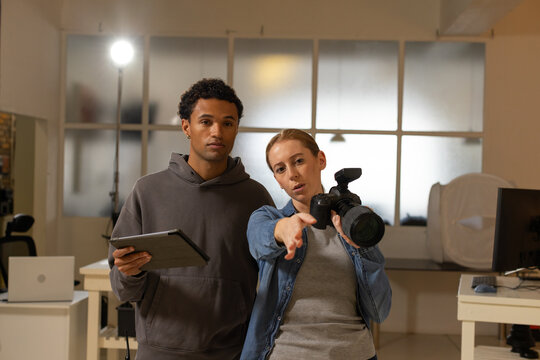 Diverse coworkers directing composition and checking tablet in photography studio with DSLR strobe