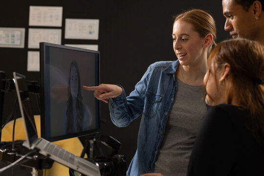 Diverse team pointing at monitor reviewing remote face on screen in studio with DSLR, copy space