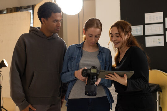 Diverse coworkers reviewing photos on DSLR camera and tablet in photography studio with softbox