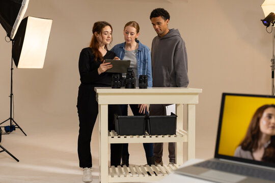 Diverse production team reviewing tablet and camera lenses on white worktable in studio